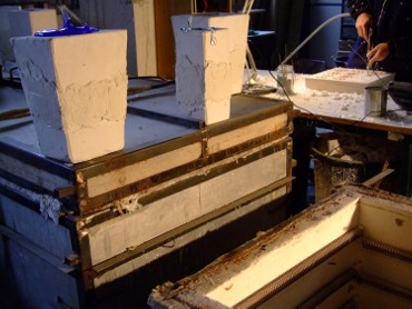 Frédéric Morin et Salomé à Saillans (26) : des moules en attente de démoulage au-dessus du petit four à pâte-de-verre. Au fond à droite, extraction du polystyrène d'un moulage de petits bougeoirs